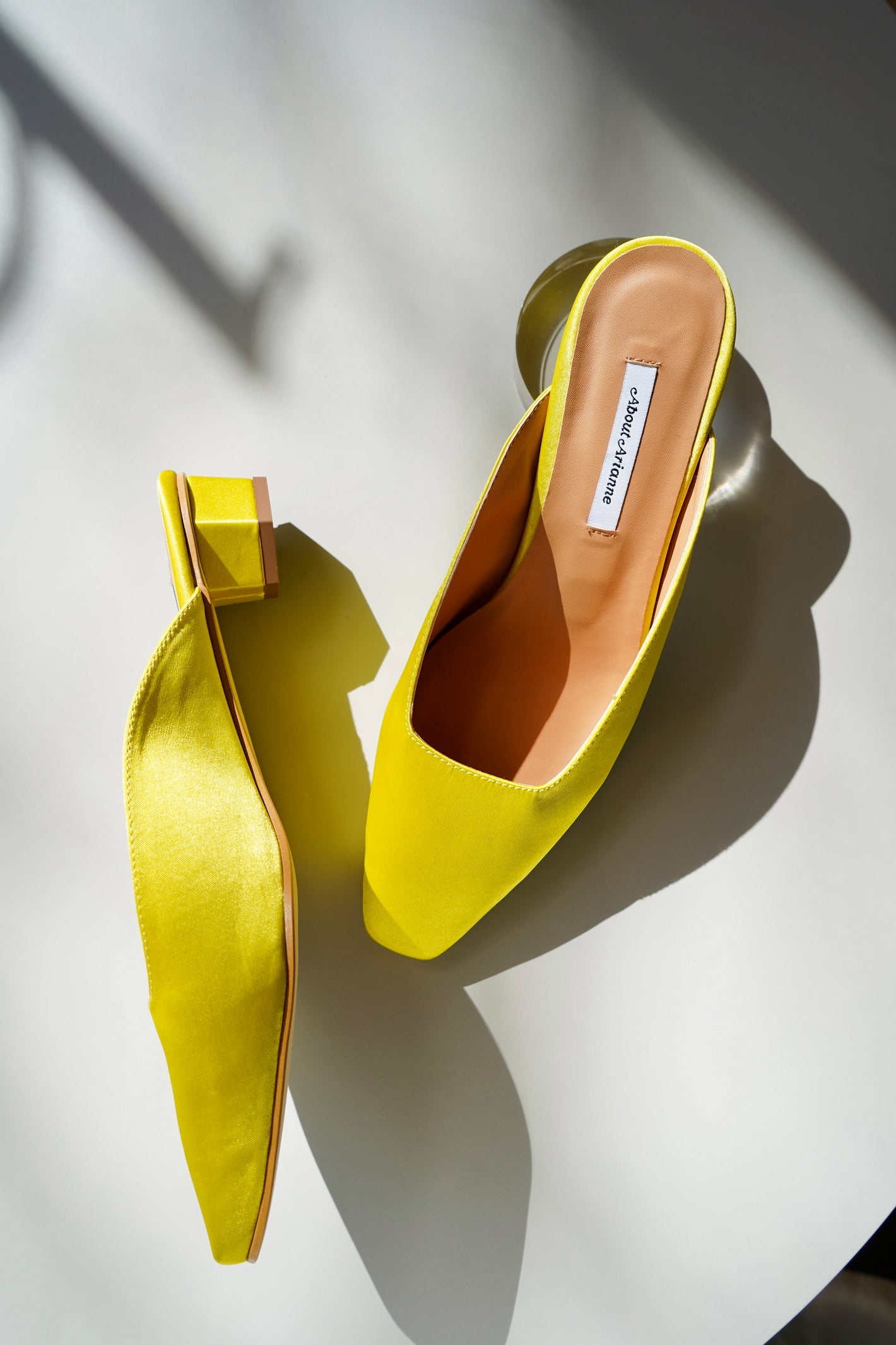 Yellow satin kitten heel mules sit on a white table in afternoon sunlight | Image by Lacey Woodroof for basic.