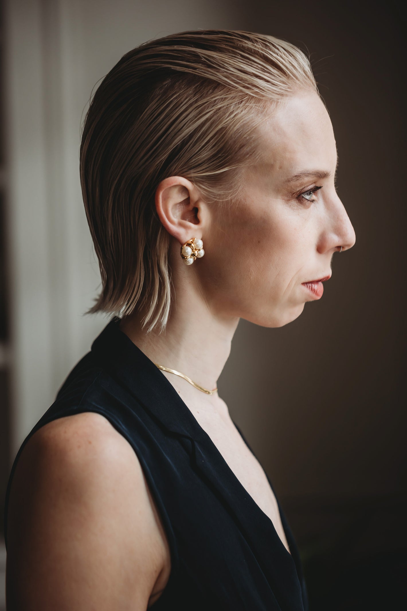 Side profile of a blonde woman wearing pears and a fitted black top | Image by Mary Fehr for basic.